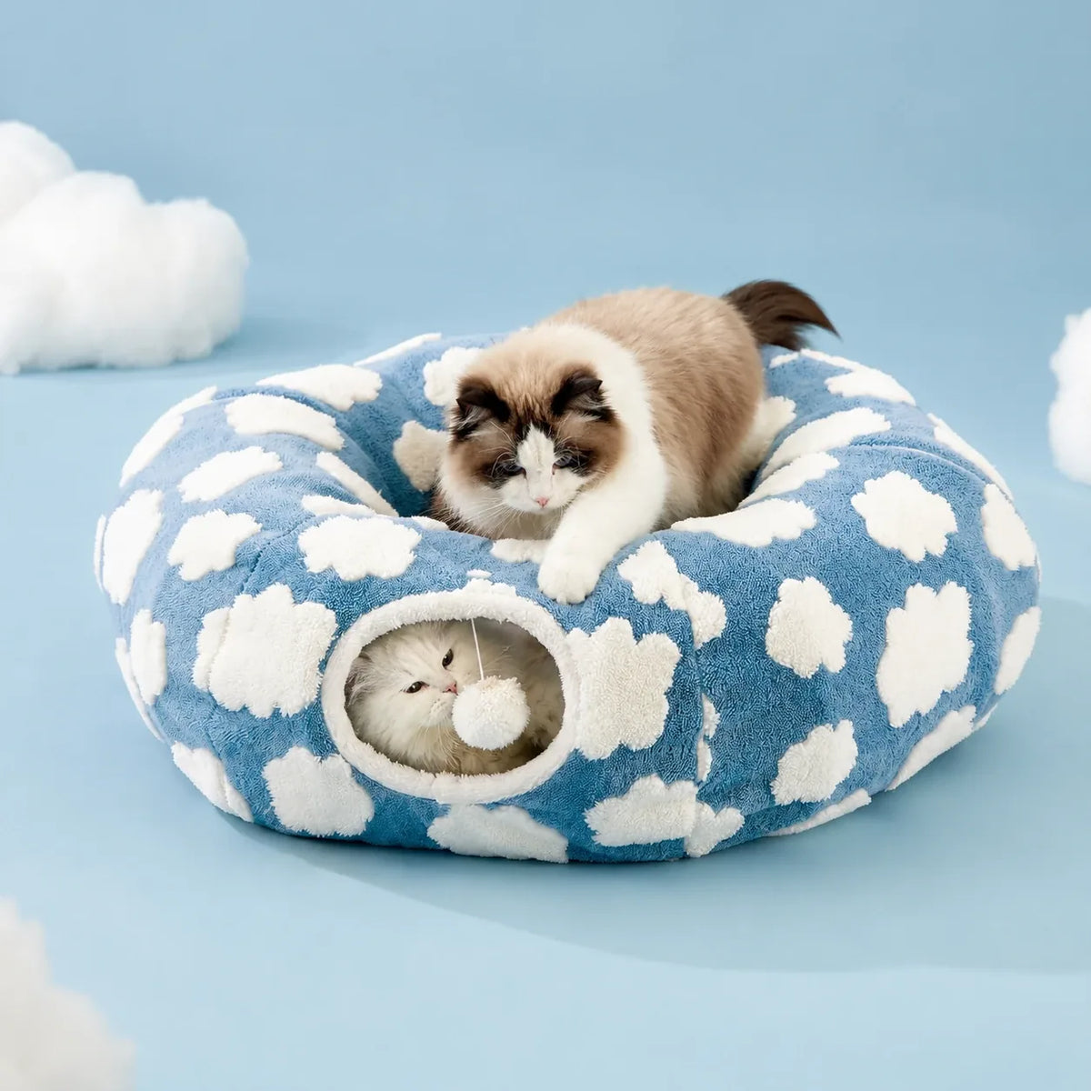 Cloud donut cat tunnel bed in sky blue with white tufted clouds, pom-pom hanging in the tunnel opening