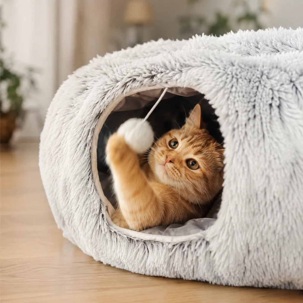 Cat batting the hanging pom-pom inside the tunnel mouth of the plush donut bed
