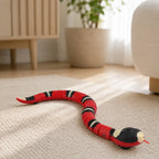 Realistic red and black scarlet kingsnake cat toy slithering across a living-room rug